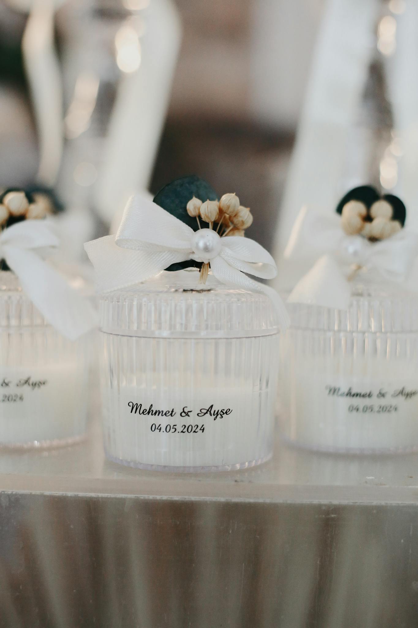 Delicate white candles in glass jars with personalized wedding labels and ribbons.