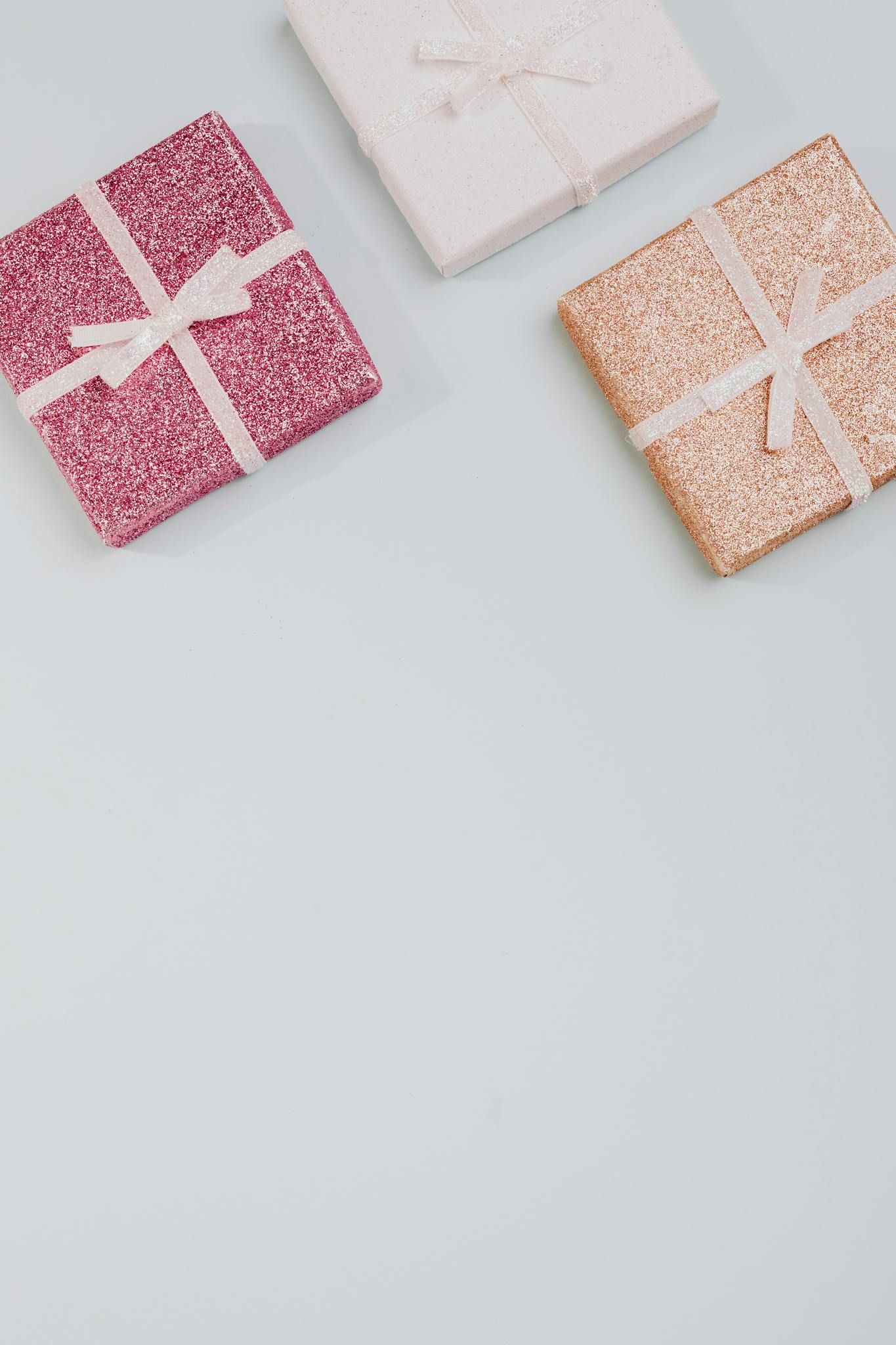 Three glittery wrapped gift boxes with ribbons on a pastel background, perfect for celebrations.